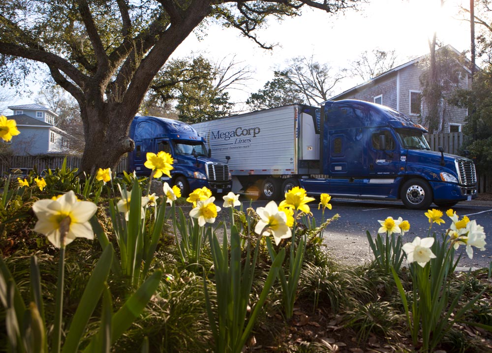 Two MegaCorp Lines trucks parked in a residential area. The sunlight is hitting a bed of glowing yellow flowers.